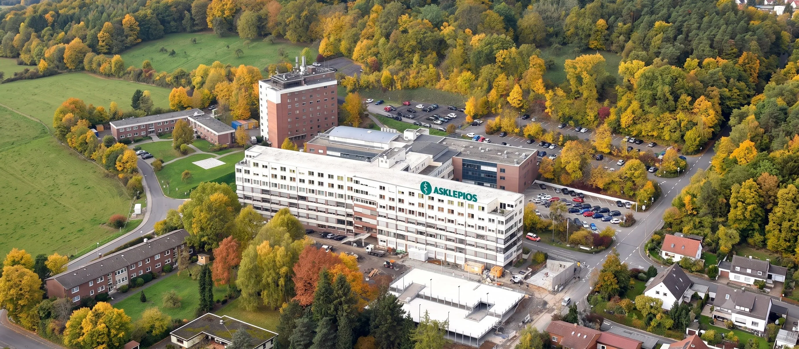 Luftaufnahme einer Asklepios-Klinik in herbstlicher Landschaft, mit dem grünen Asklepios-Schriftzug auf dem Gebäude