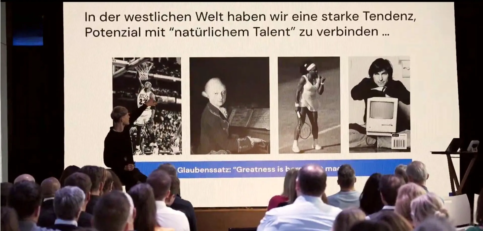 Speaker hält einen Impuls vor Publikum, im Hintergrund die Folie „Glaubenssatz: Greatness is born or made“