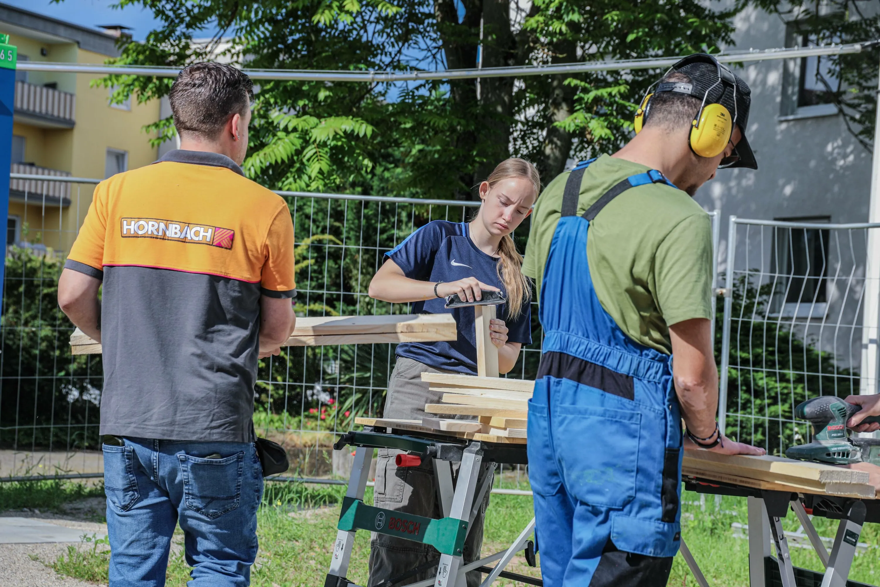 Jugendliche schleifen und bearbeiten Holz gemeinsam mit einem HORNBACH-Mentor im Workshop